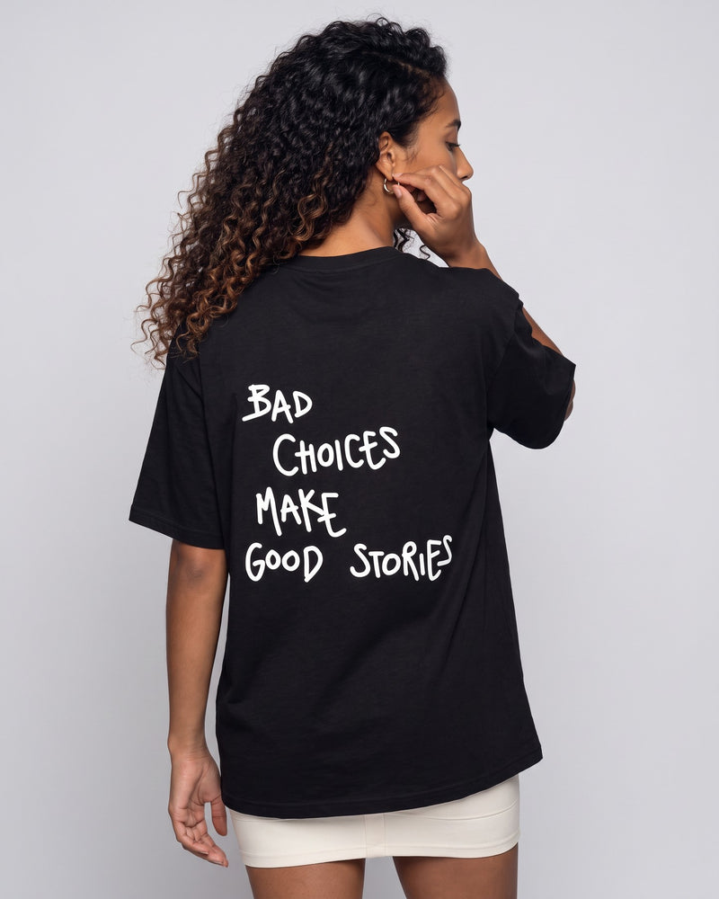 Camiseta oversized feminina MALTA® bad choices preta vista de costas no estúdio, com a frase “bad choices make good stories”