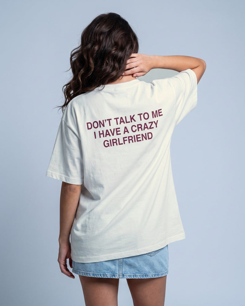 Camiseta oversized feminina MALTA® crazy girlfriend off-white vista de costas no estúdio, com a frase “don't talk to me, i have a crazy girlfriend”