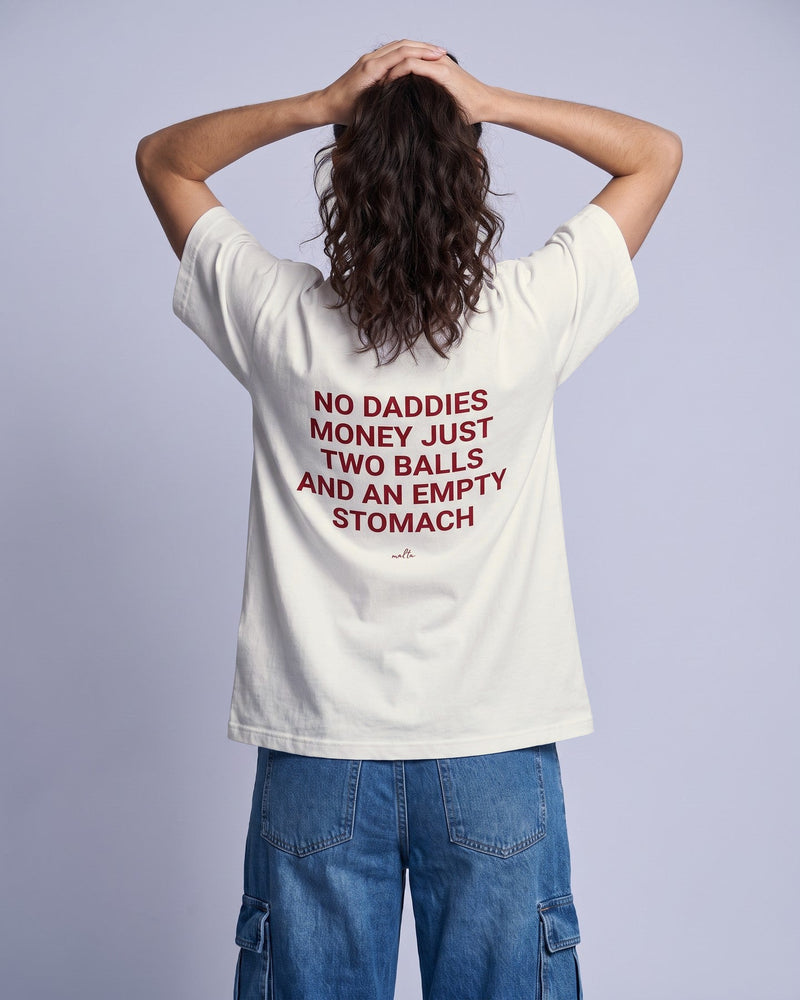 Camiseta oversized feminina MALTA® no daddies money off-white vista de costas no estúdio, com a frase “no daddies money just two balls and an empty stomach”