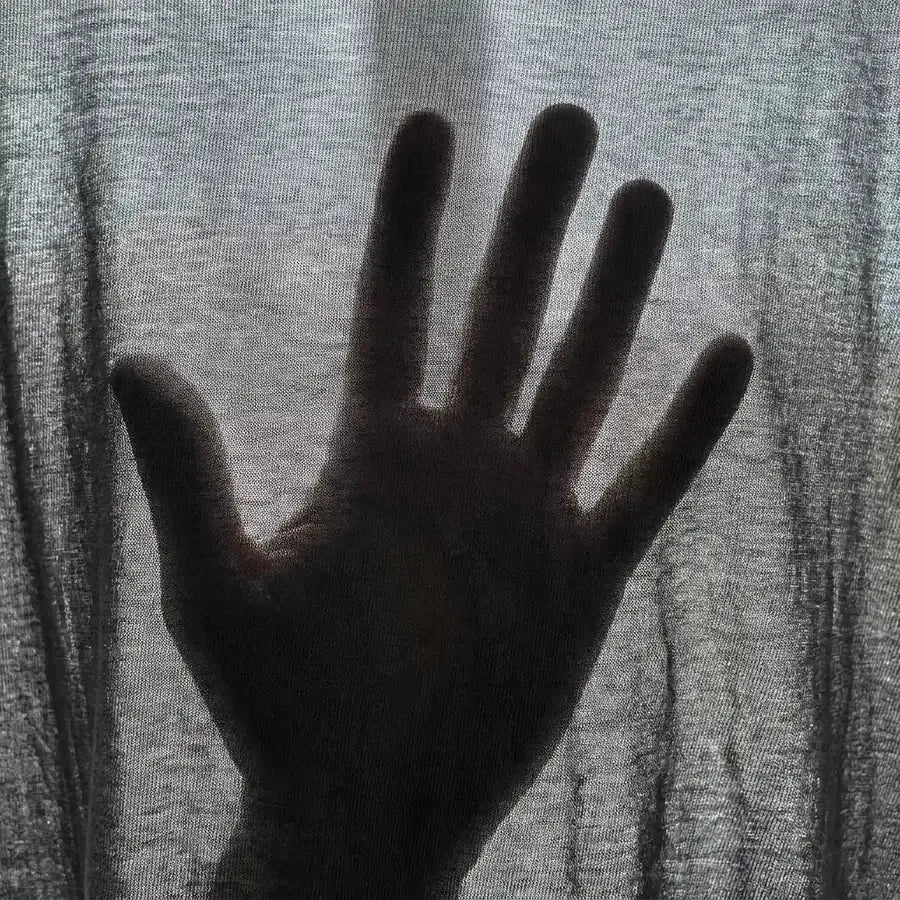 Mão atrás de uma malha fina contra a luz: contra a luz, o preto vira cinza e a mão aparece.
