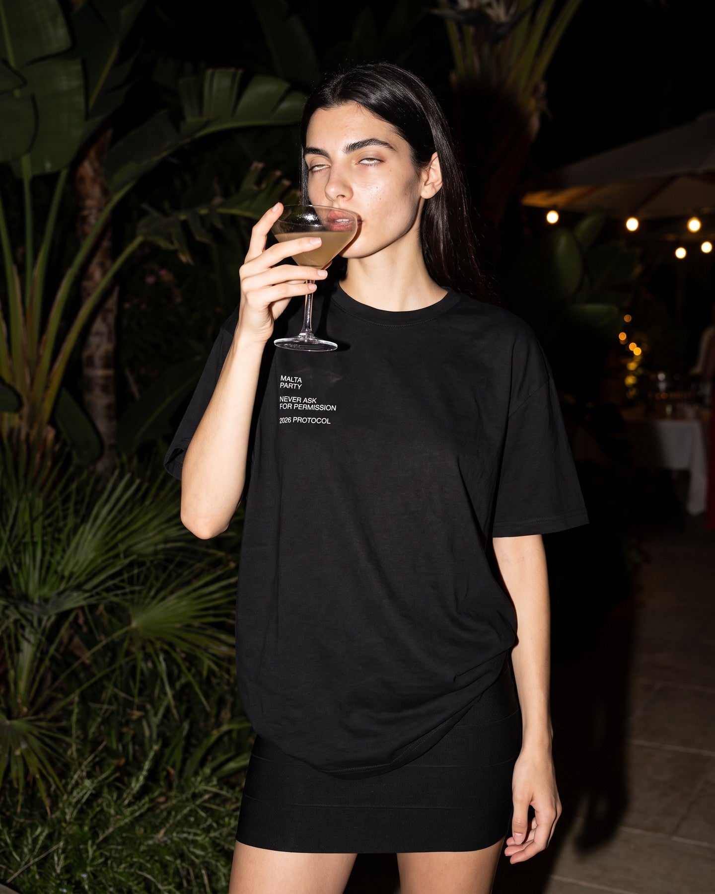 Mulher usando a camiseta oversized MALTA® after party preta num terraço à noite