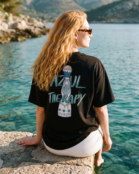 Mulher de costas usando a camiseta oversized MALTA® azul therapy preta num cais sobre água turquesa