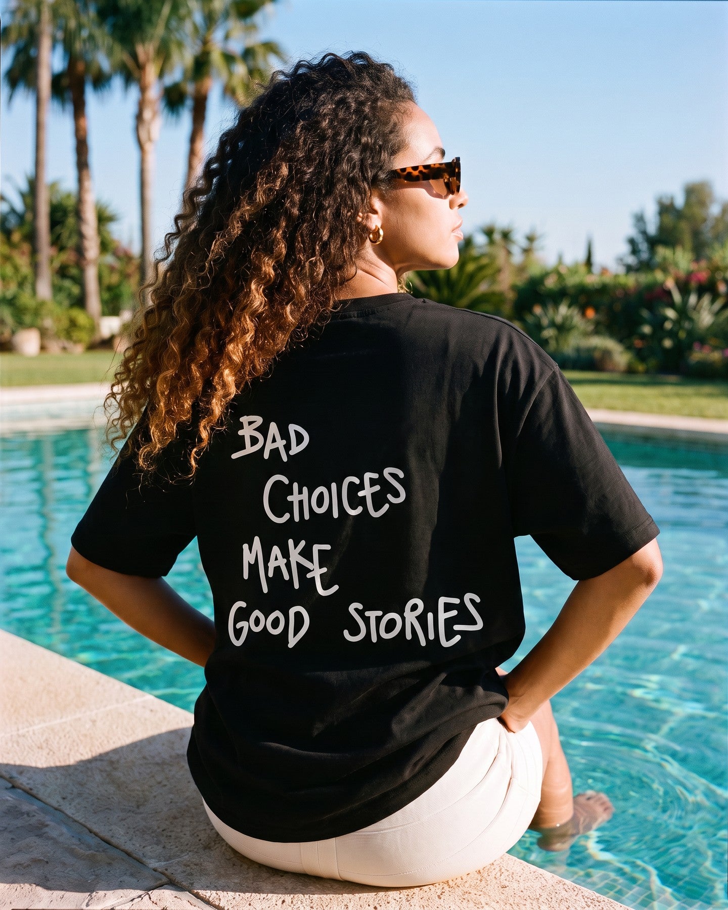 Mulher de costas usando a camiseta oversized MALTA® bad choices preta na borda de uma piscina