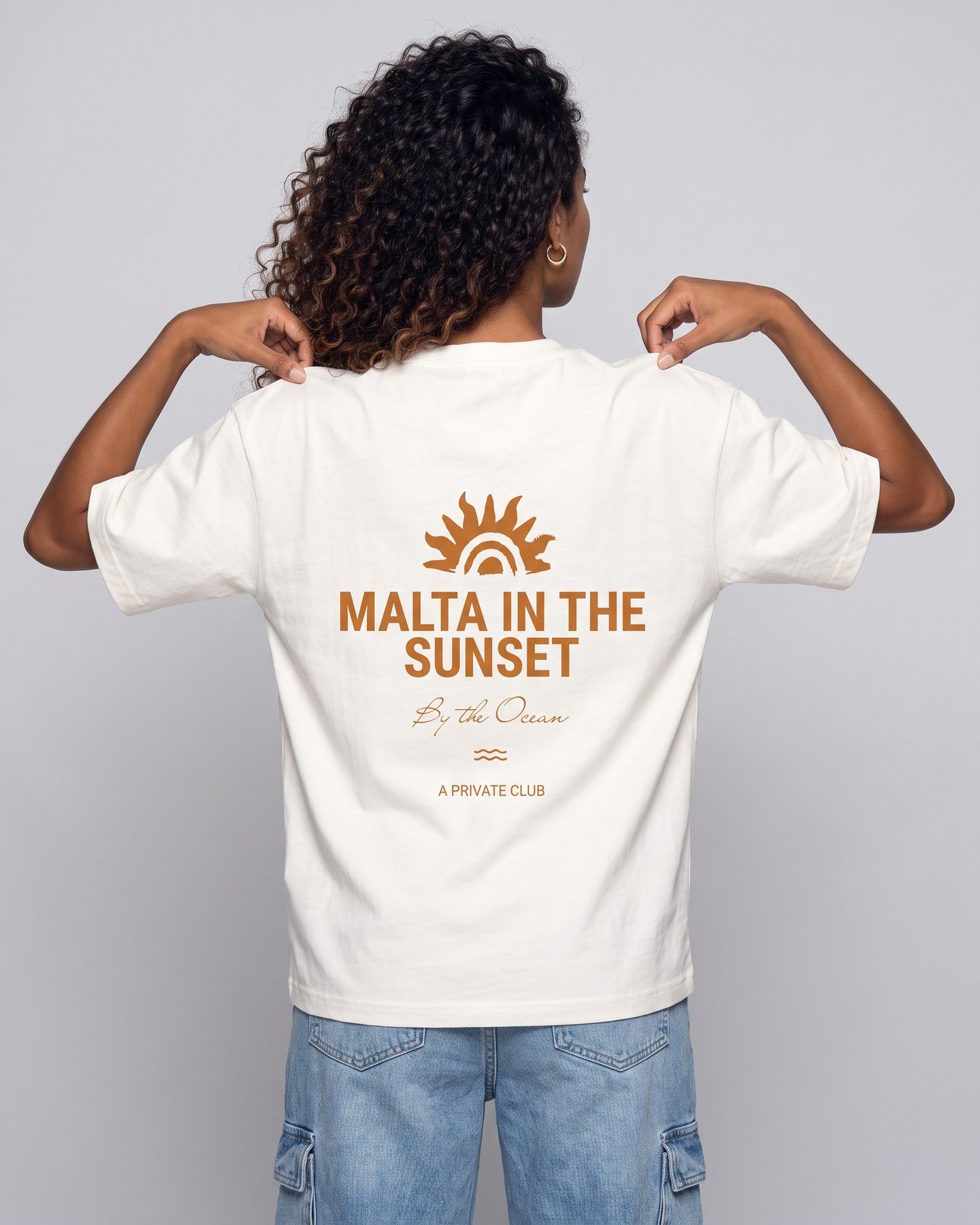 Camiseta oversized feminina MALTA® innerbloom off-white vista de costas no estúdio, com a frase “malta in the sunset”