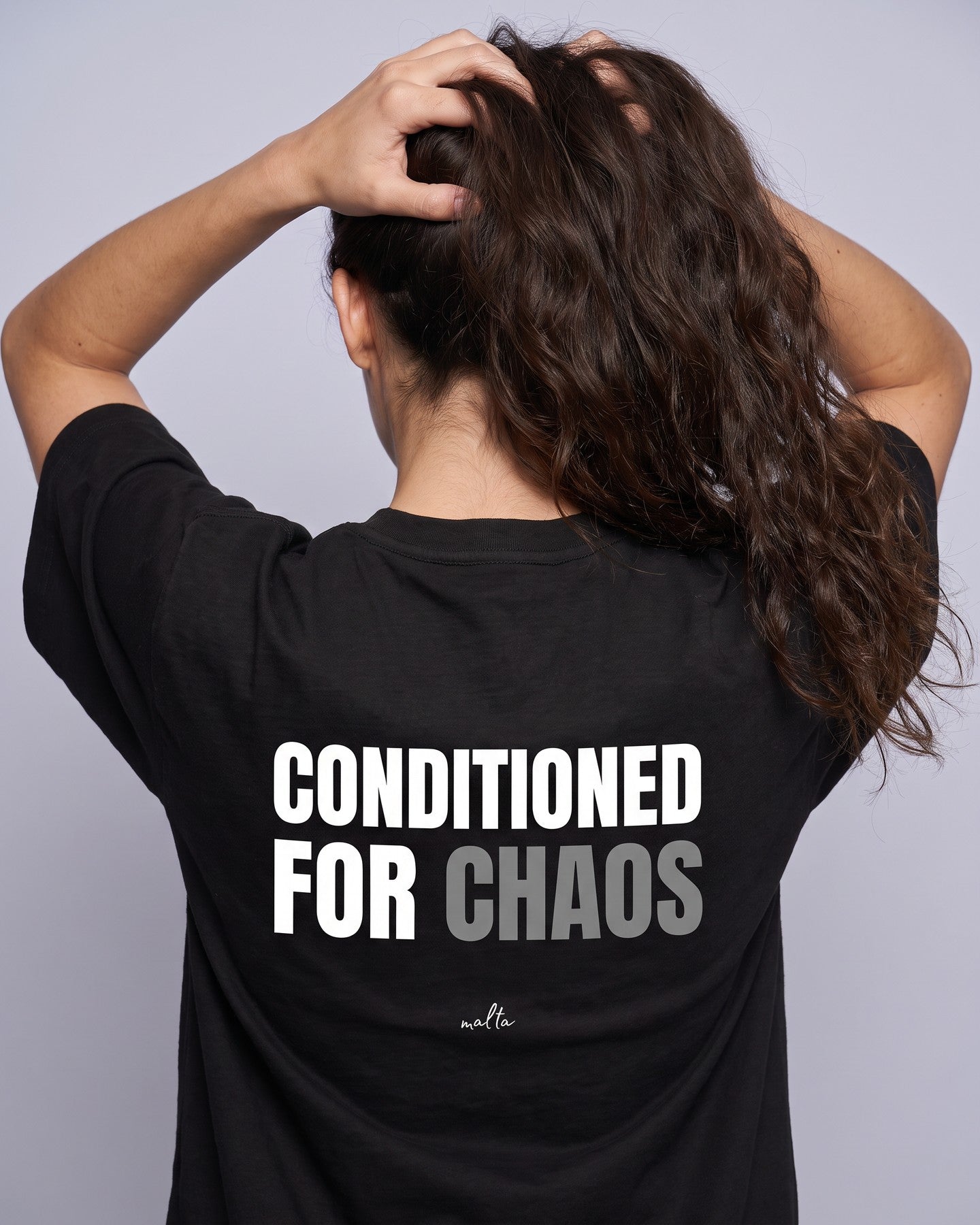 Detalhe da camiseta oversized MALTA® conditioned for chaos preta no corpo feminino