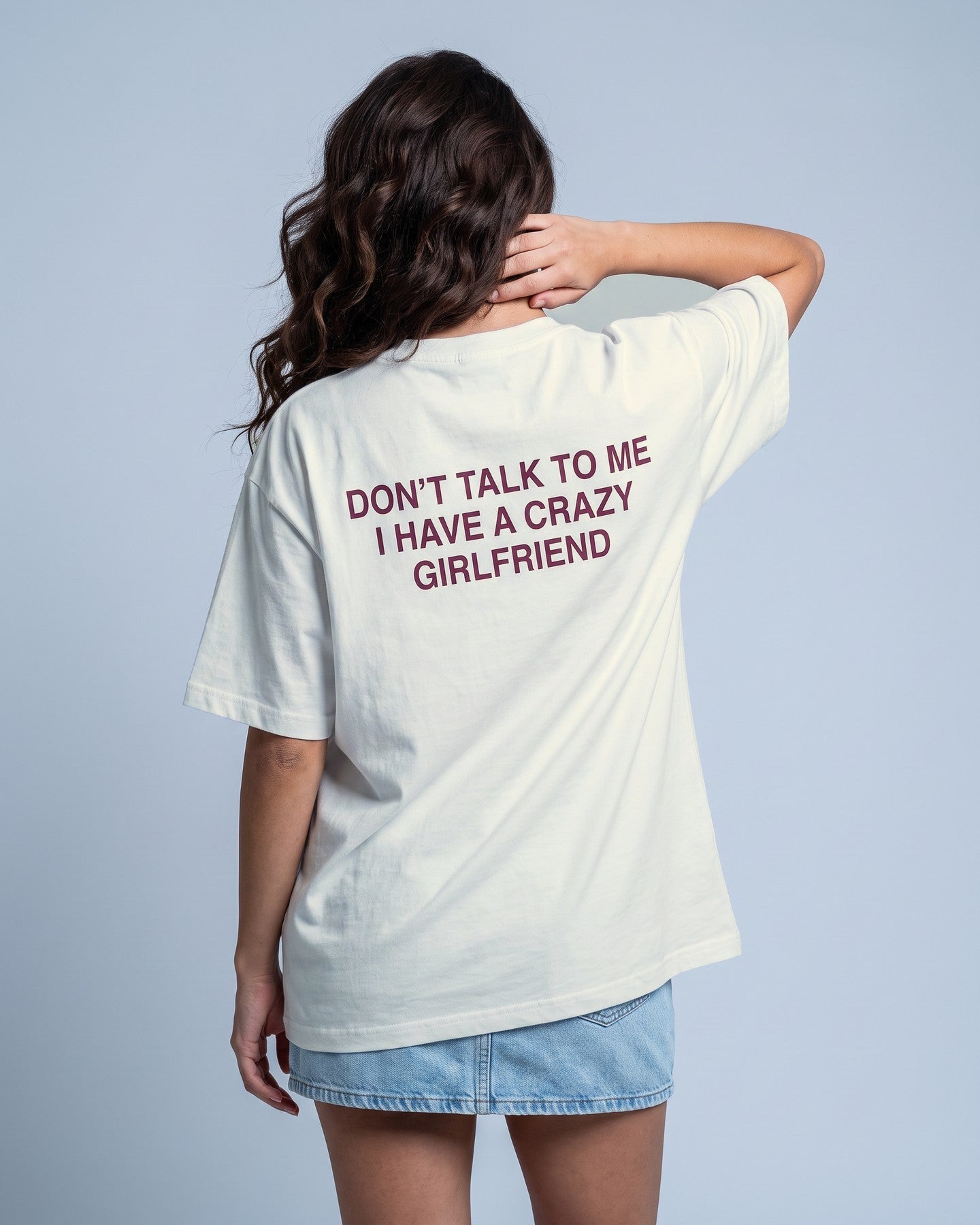 Camiseta oversized feminina MALTA® crazy girlfriend off-white vista de costas no estúdio, com a frase “don't talk to me, i have a crazy girlfriend”