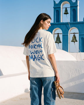 Mulher de costas usando a camiseta oversized MALTA® i want magic off-white num terraço caiado de ilha grega