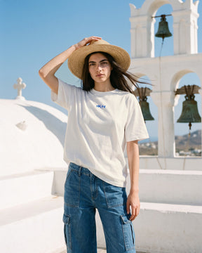 Mulher usando a camiseta oversized MALTA® i want magic off-white num terraço caiado de ilha grega