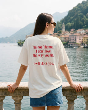 Mulher de costas usando a camiseta oversized MALTA® i will block you off-white na balaustrada de uma villa no lago