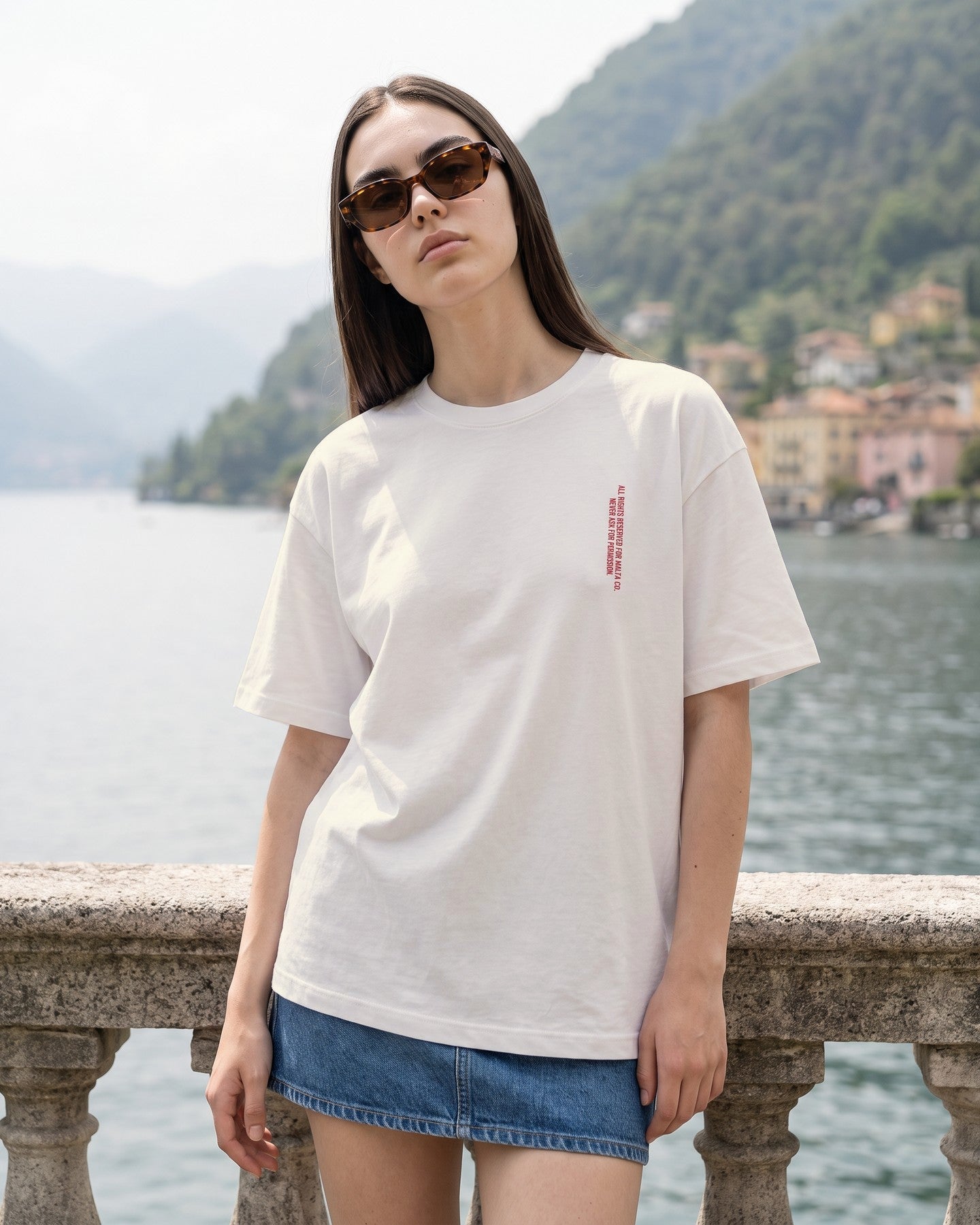 Mulher usando a camiseta oversized MALTA® i will block you off-white na balaustrada de uma villa no lago