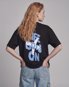 Camiseta oversized feminina MALTA® life goes on preta vista de costas no estúdio, com a frase “life goes on”
