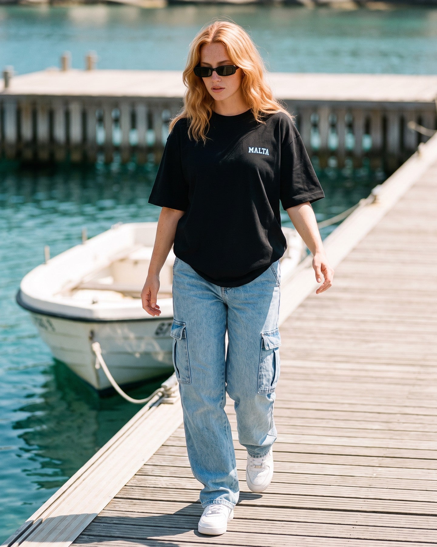 Mulher usando a camiseta oversized MALTA® life goes on preta num píer sobre água turquesa