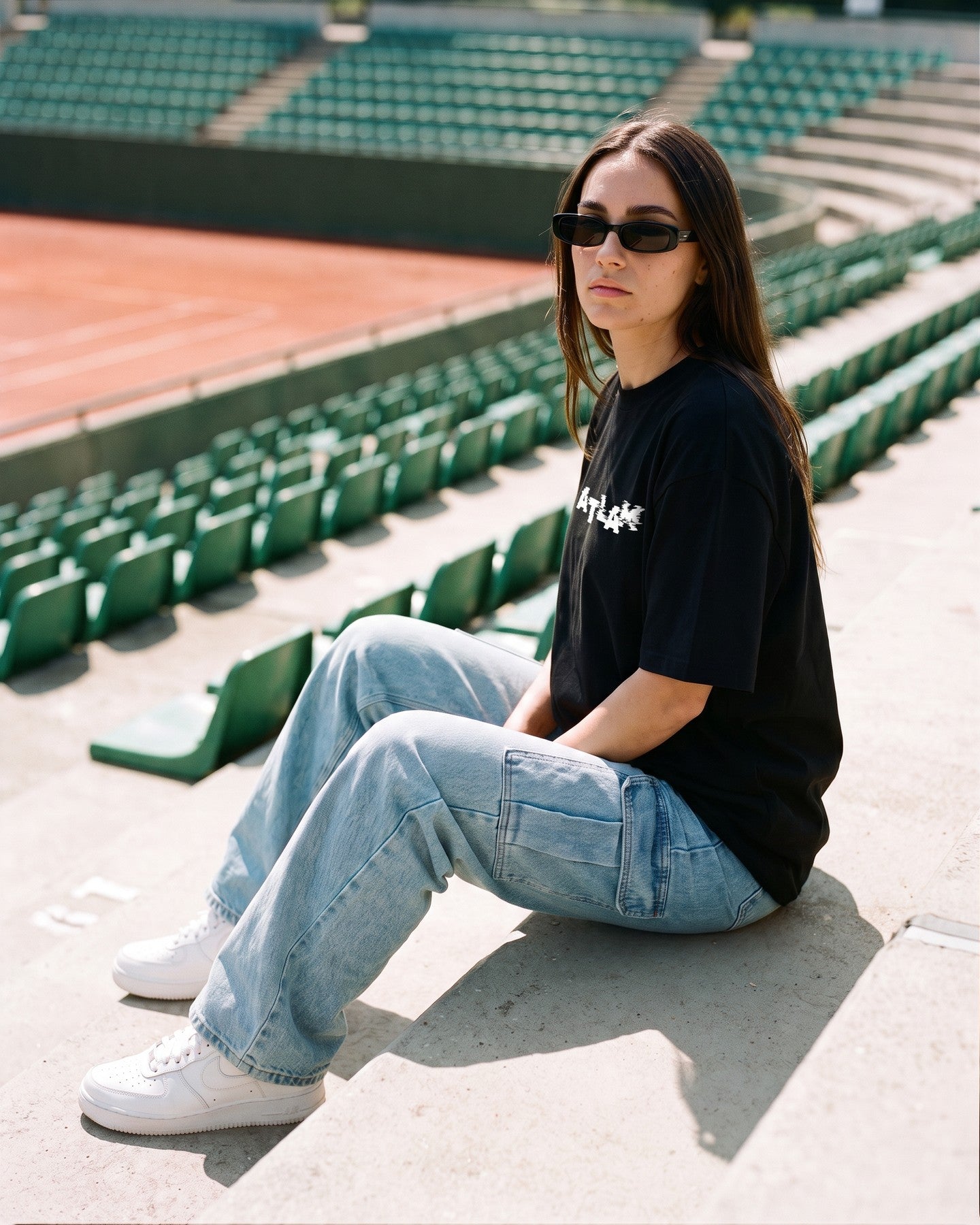 Mulher usando a camiseta oversized MALTA® life is a simulation preta na arquibancada de um clube de tênis