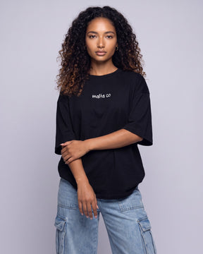 Camiseta oversized feminina MALTA® need money for porsche preta vestida de frente, no estúdio