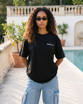 Mulher usando a camiseta oversized MALTA® need money for porsche preta no terraço de um clube na Riviera