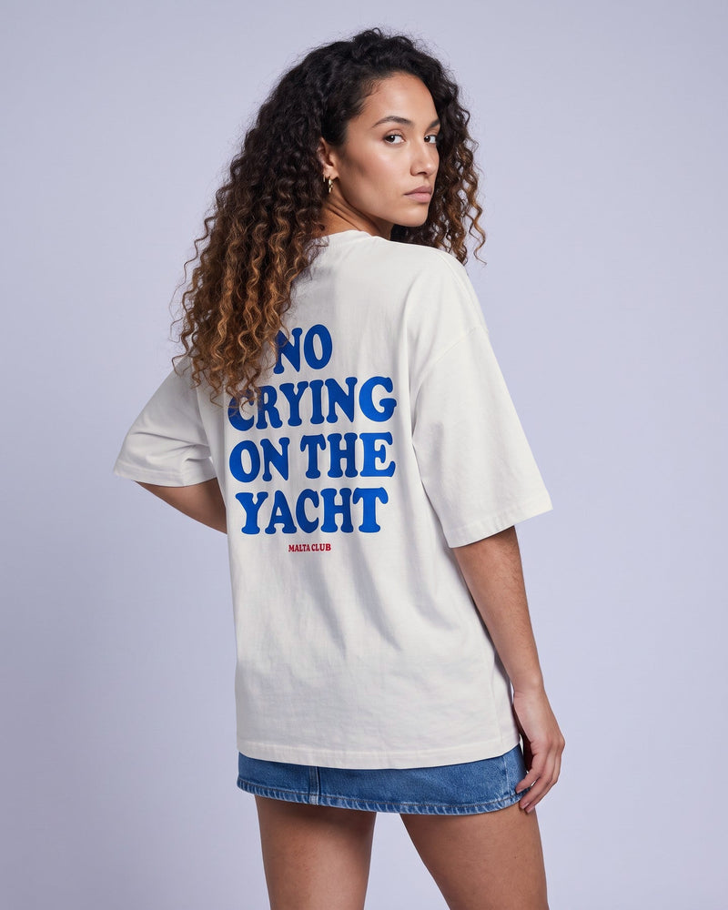 Camiseta oversized feminina MALTA® no crying on the yacht off-white vista de costas no estúdio, com a frase “no crying on the yacht”