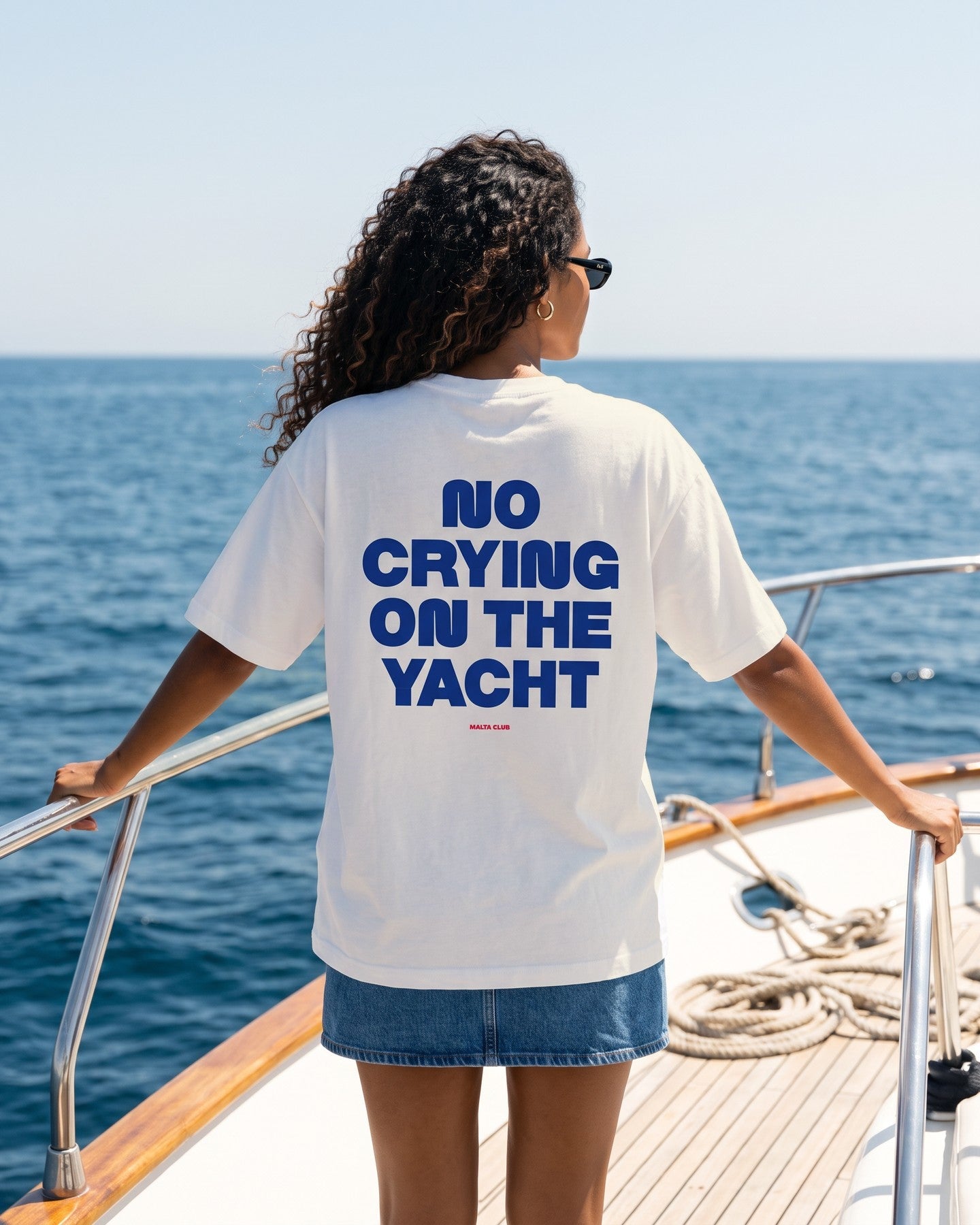 Mulher de costas usando a camiseta oversized MALTA® no crying on the yacht off-white no convés de um iate