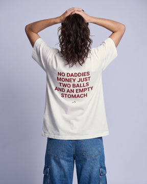 Camiseta oversized feminina MALTA® no daddies money off-white vista de costas no estúdio, com a frase “no daddies money just two balls and an empty stomach”