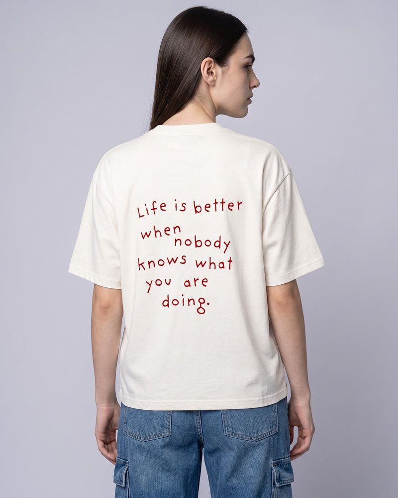 Camiseta oversized feminina MALTA® nobody knows off-white vista de costas no estúdio, com a frase “life is better when nobody knows what you are doing.”
