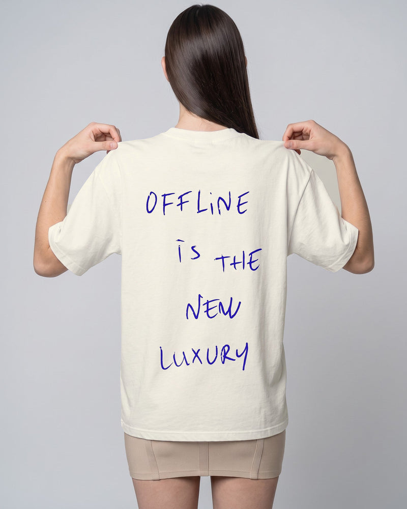 Camiseta oversized feminina MALTA® offline luxury off-white vista de costas no estúdio, com a frase “offline is the new luxury”