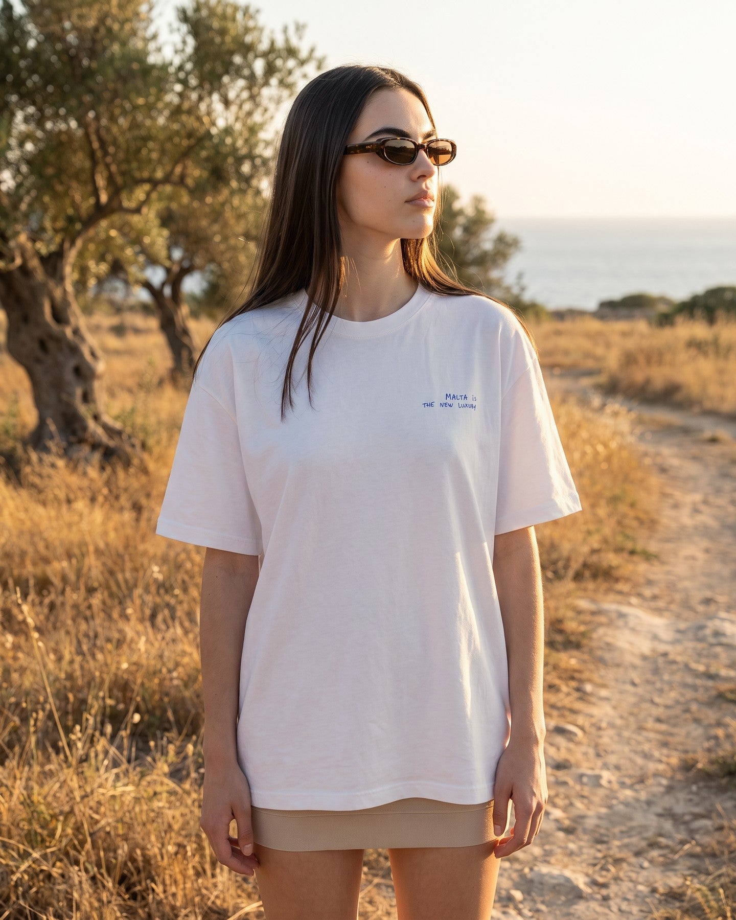 Mulher usando a camiseta oversized MALTA® offline luxury off-white num campo com oliveiras