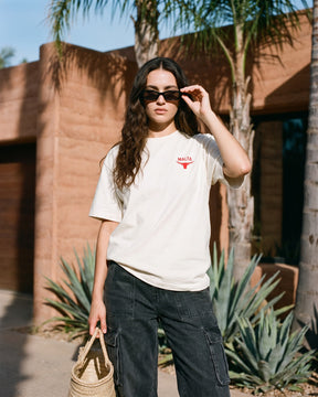 Mulher usando a camiseta oversized MALTA® red flags off-white diante de uma casa terracota com palmeiras