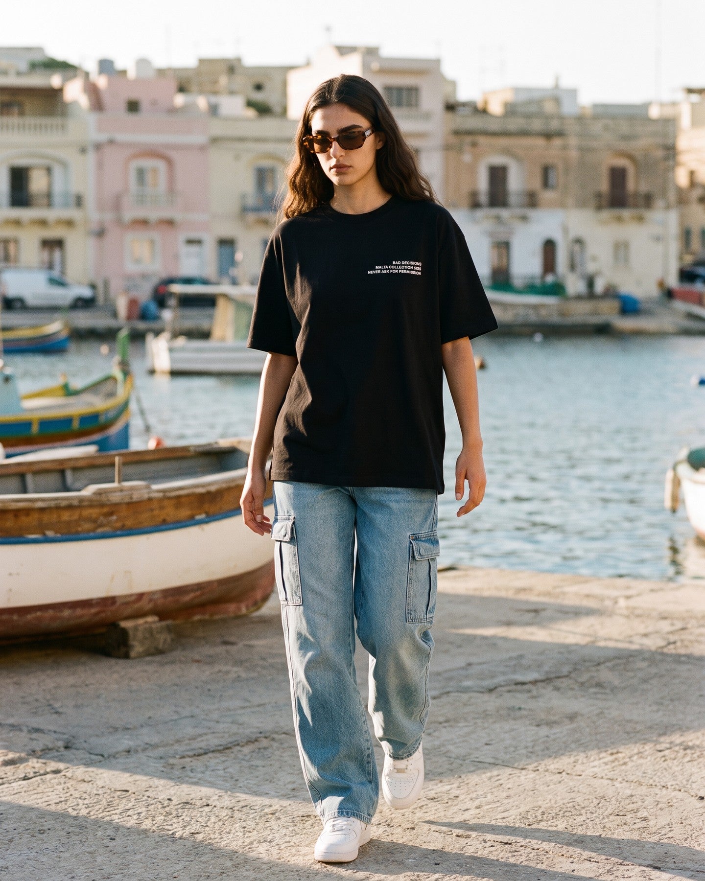 Mulher usando a camiseta oversized MALTA® bad decisions preta numa vila de pescadores