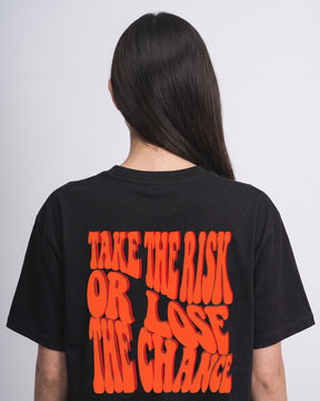 Detalhe da camiseta oversized MALTA® take the risk preta no corpo feminino