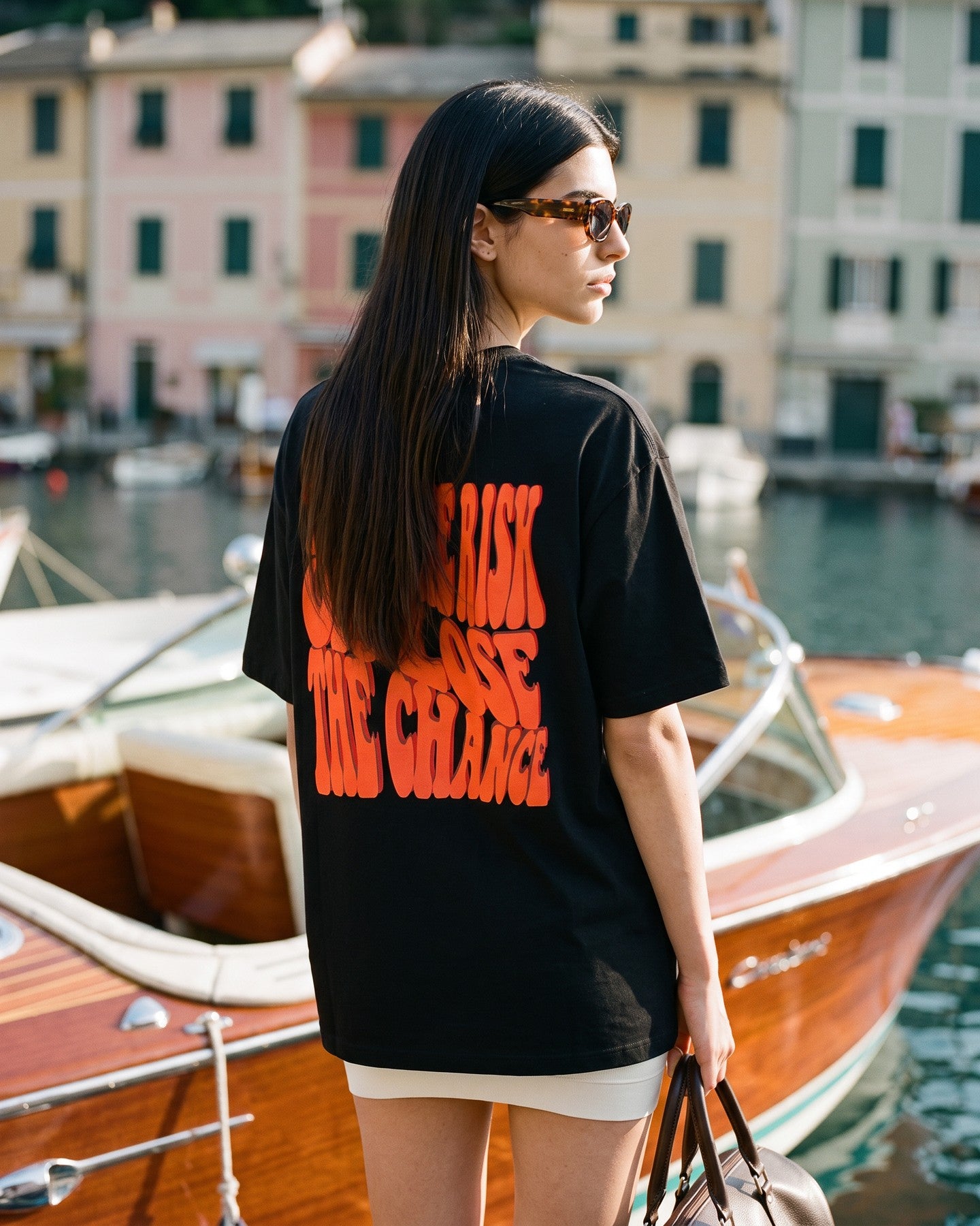 Mulher de costas usando a camiseta oversized MALTA® take the risk preta numa lancha clássica de madeira