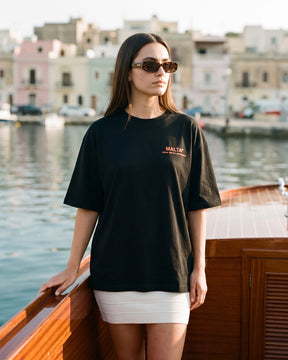 Mulher usando a camiseta oversized MALTA® take the risk preta numa lancha clássica de madeira