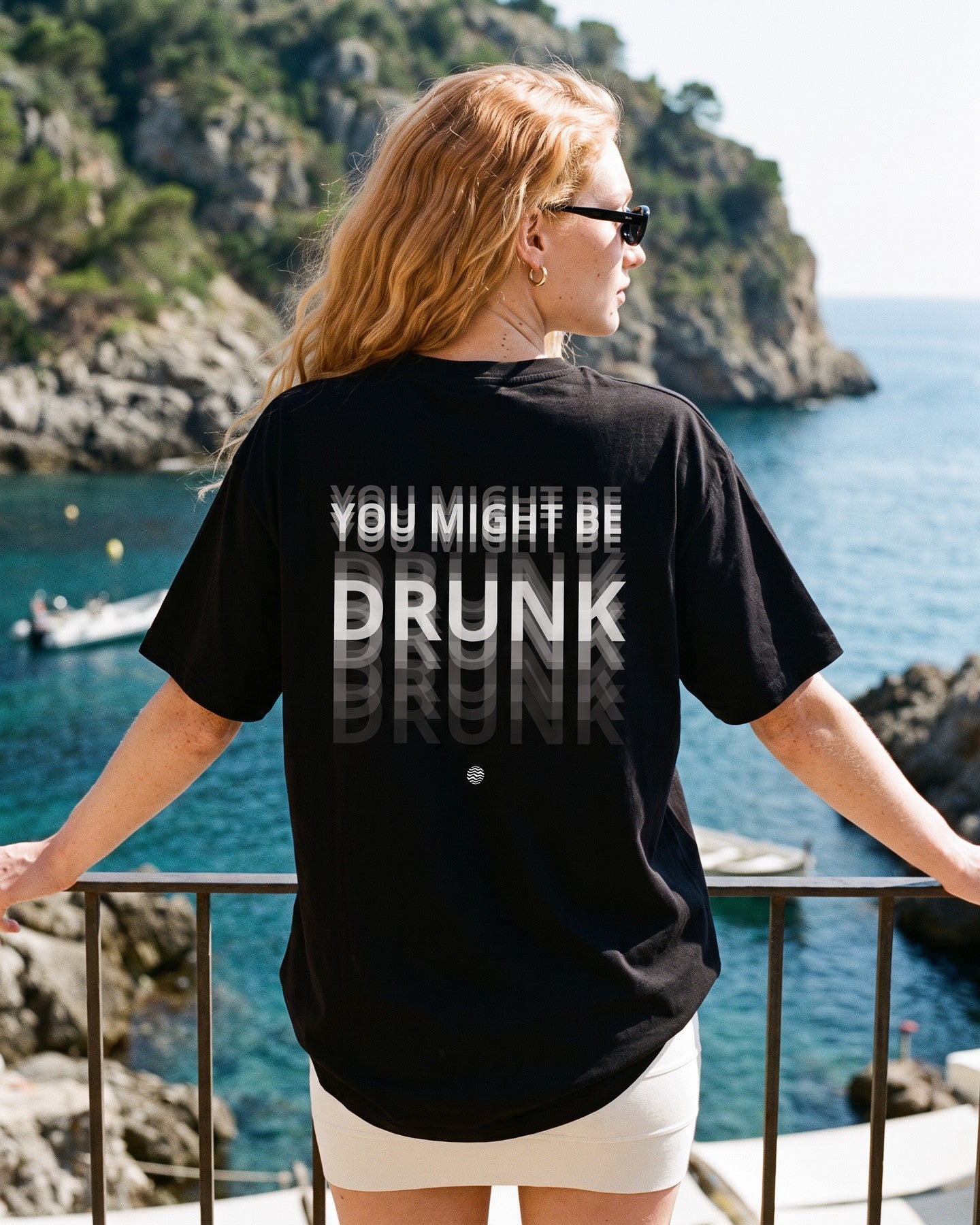 Mulher de costas usando a camiseta oversized MALTA® you might be drunk preta numa sacada sobre o mar
