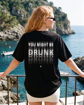 Mulher de costas usando a camiseta oversized MALTA® you might be drunk preta numa sacada sobre o mar
